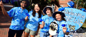 A group of students, smiling and wearing blue, standing in front of a sign that reads "Welcome, new Jays!"