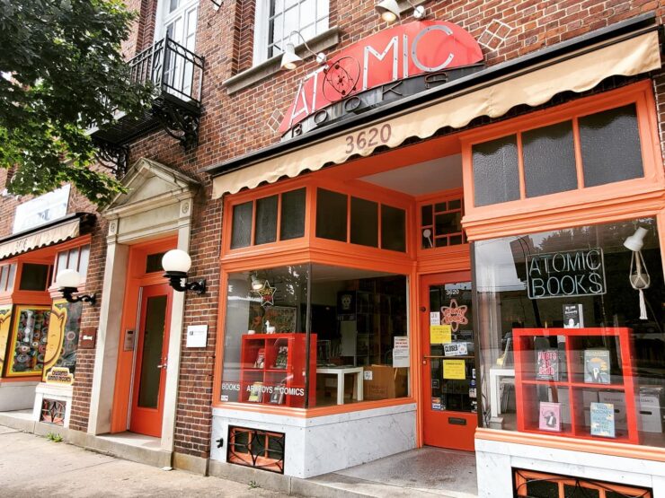 Exterior view of bookstore, painted red with a yellow awning and a sign that reads "Atomic".