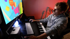 A student sitting a computer with a piano keyboard