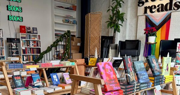 Tables in a bookstore filled with books. A sign that reads "Greedy Reads" hangs on the wall.