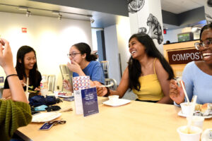 A group of students sitting at a table, sharing a meal and laughing with one another.