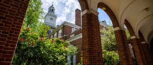 A brick path, lined with archwways, and a clock tower in the background.