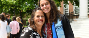 A student, wearing graduation robe, poses with mother