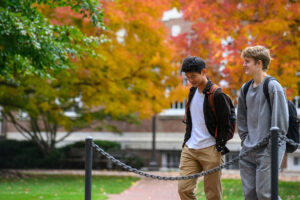 Two students walking across a campus quad with bright fall leaves in the background