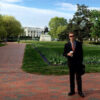 A student, wearing a suit, stands in front of the White House